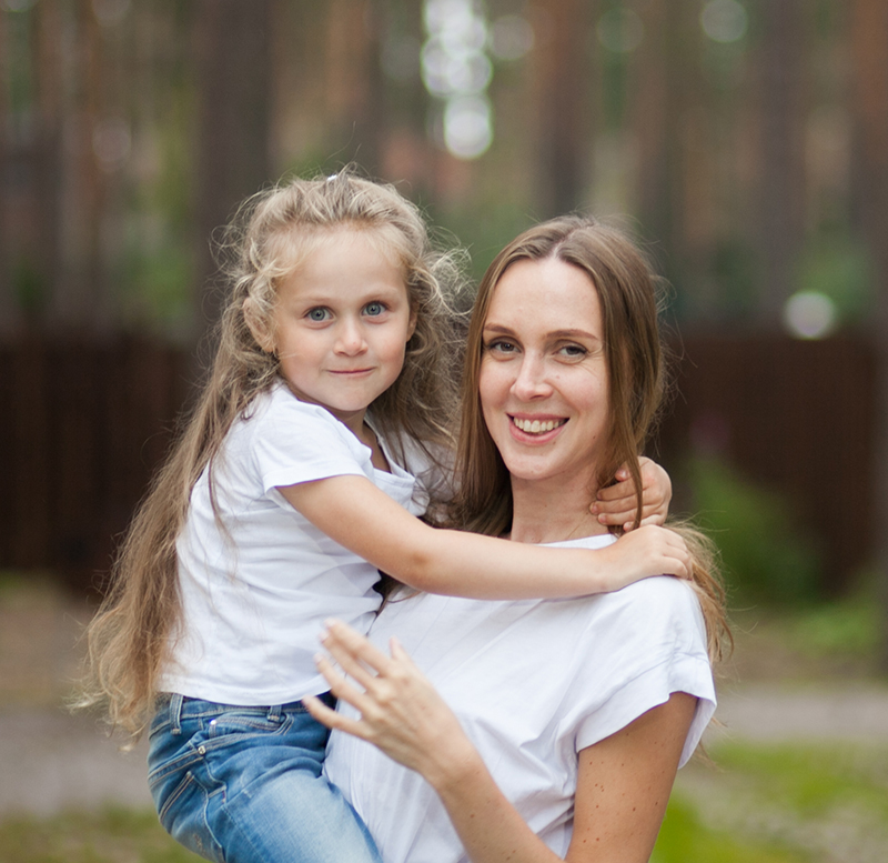 Happy smiling mother and her cute emotional little daughter child in white shirts and denim jeans are hugging and having fun outdoor in nature at countryside. Spending summer time with family.